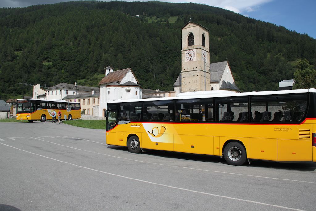 Yellow postal buses stop in front of St John's Monastery in Müstair, Switzerland